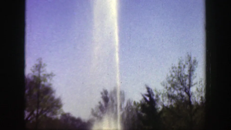 1949 Cincinnati home-movie frame showing a large fountain spray rising above trees and greenery.