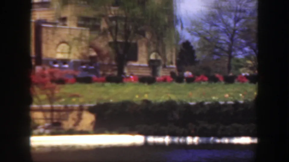 1949 Cincinnati 8mm still showing part of a stone mansion, manicured lawn, red flower beds, trees, and reflected water.