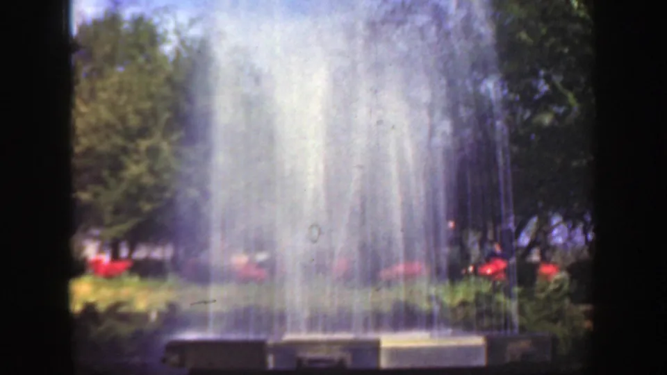 The fountain spray dominates this 1949 Cincinnati park view, with the basin, red flowers, greenery, and trees softened by 8mm grain.