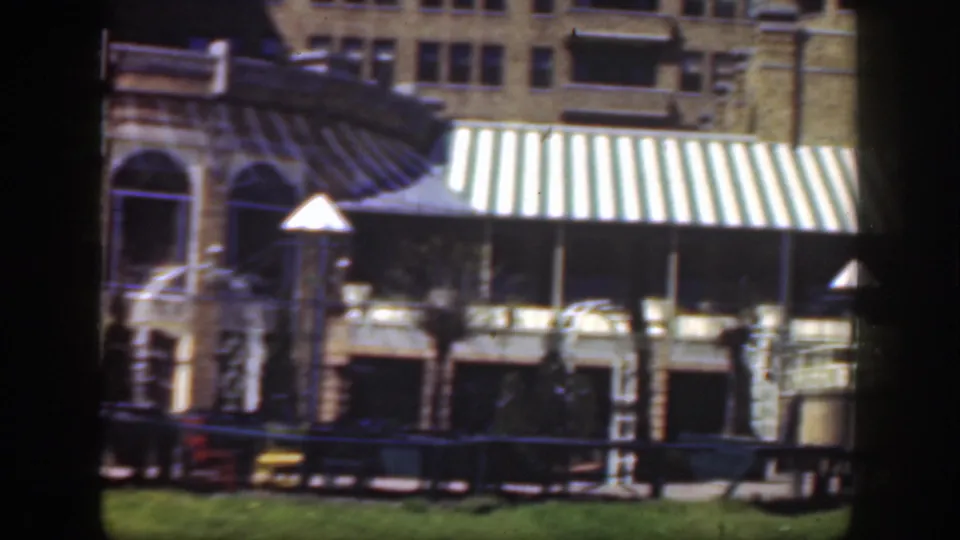 1949 Cincinnati exterior view of a formal building with striped awning, arched window, railings, benches and cars near the curb.