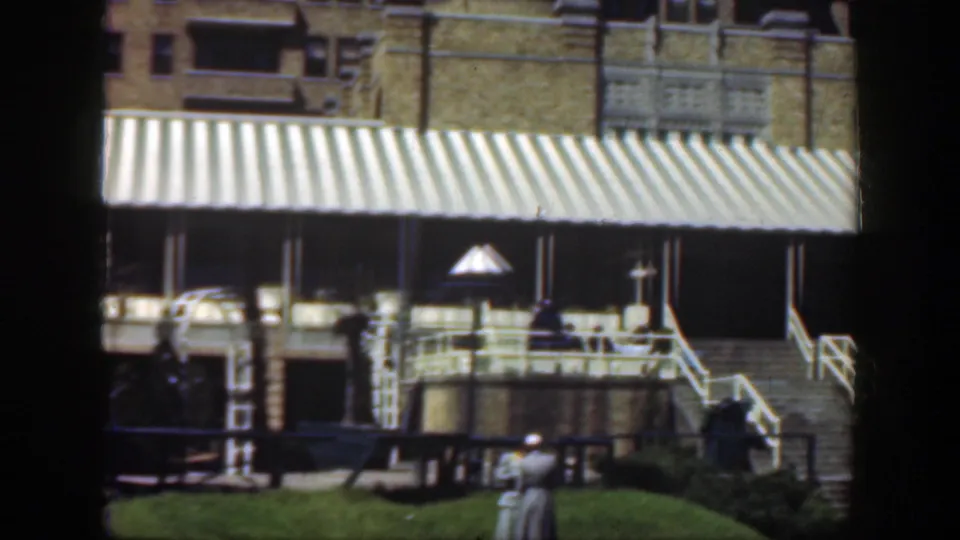 1949 Cincinnati 8mm frame showing a striped awning, broad steps, lawn, benches and distant pedestrians near the building.