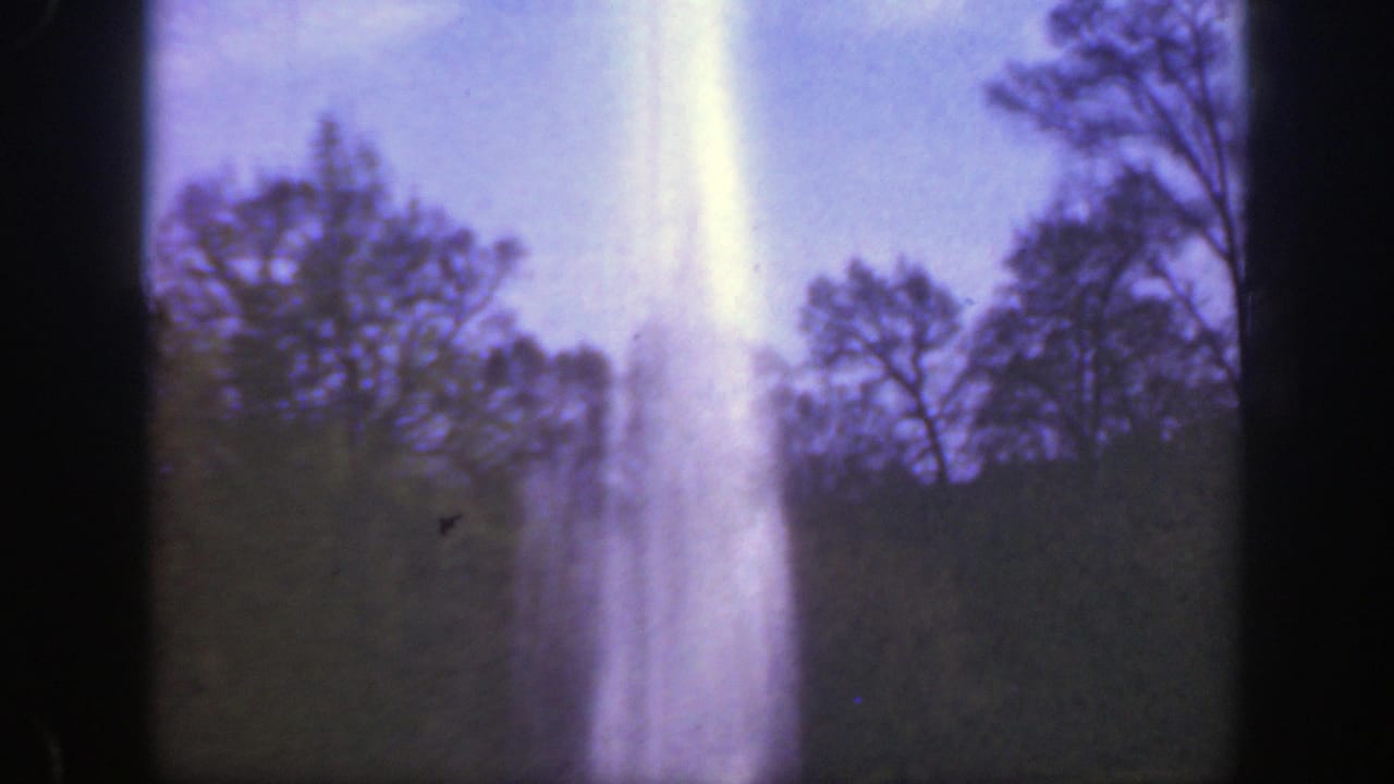 Fountain plume centered against trees and blue sky.