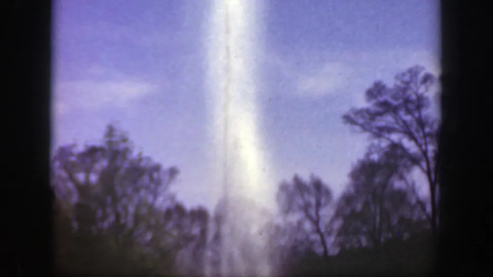 1949 Cincinnatti, Ohio 8mm frame with a bright fountain column above a low line of trees in a sunny outdoor setting.