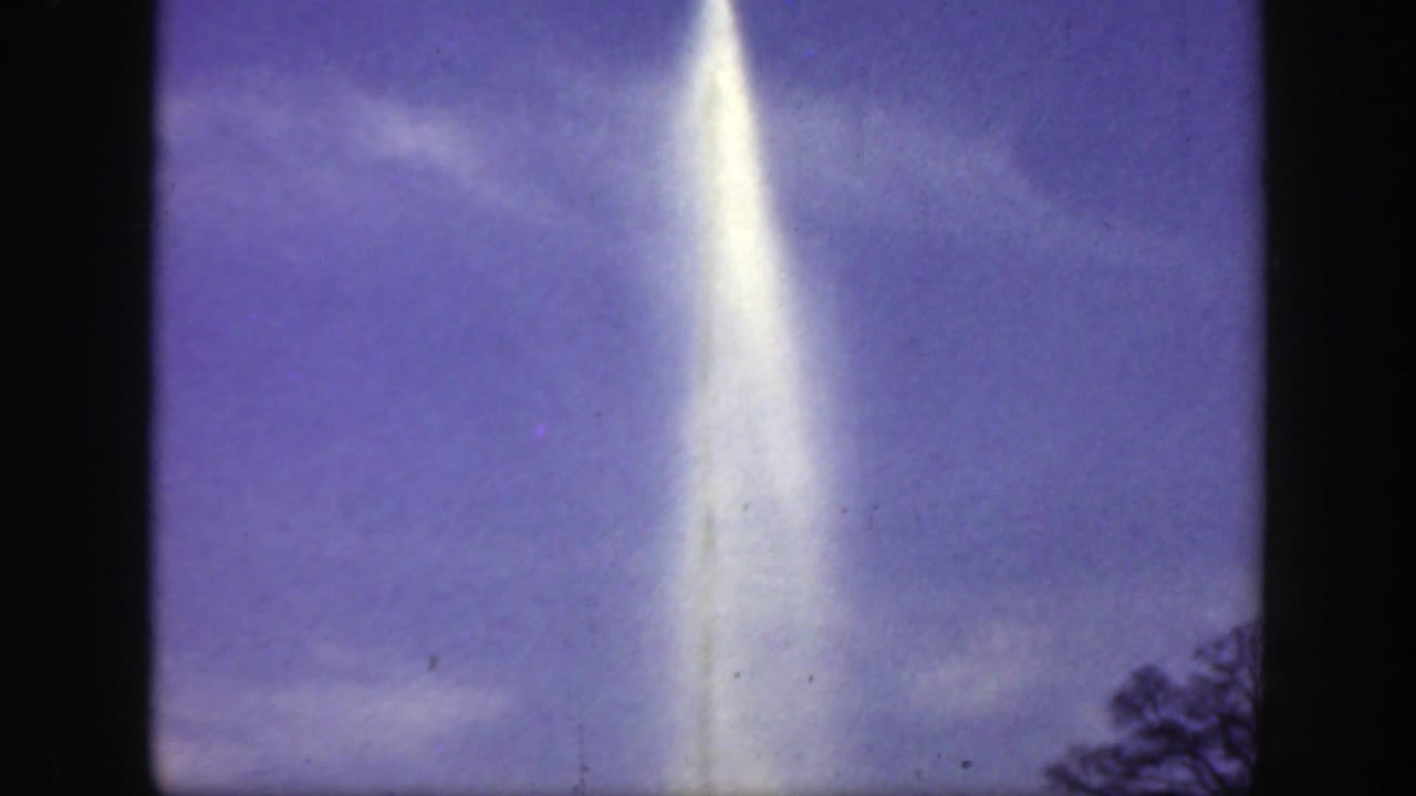 Bright water plume rising into a purple-blue sky with faint clouds and dark film borders.