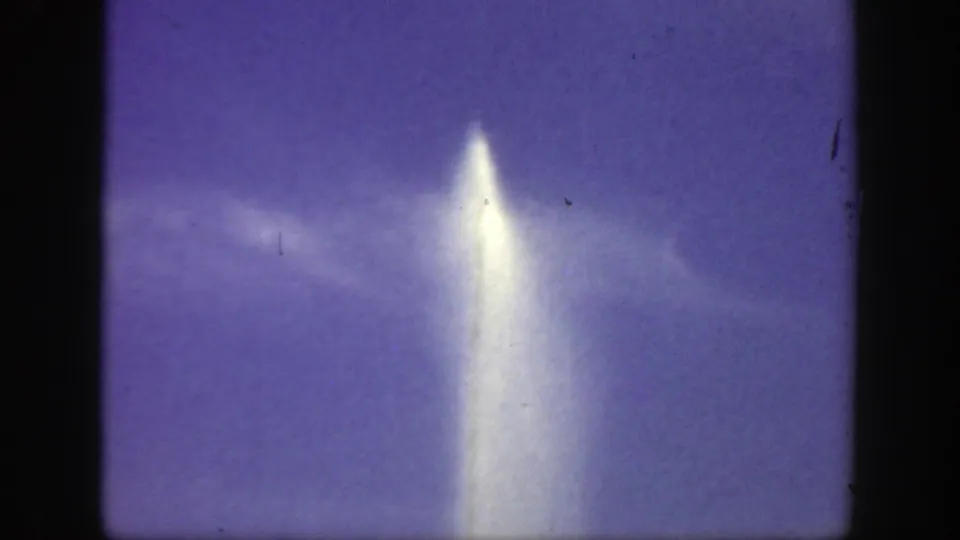 The water jet appears near the center of a 1949 Cincinnati 8mm frame, glowing against blue-purple sky and faint cloud bands with no people visible.