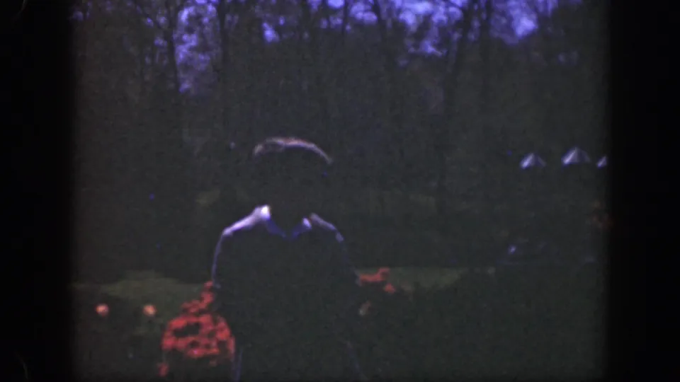 In 1949 Cincinnati home-movie footage, a shadowed young person walks toward the camera past red garden flowers.
