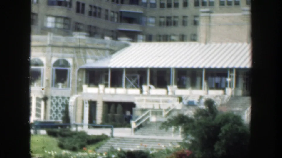 1949 Cincinnati 8mm frame focused on the building's covered entrance, broad staircase, lower facade, shrubs, and small distant people near the steps.
