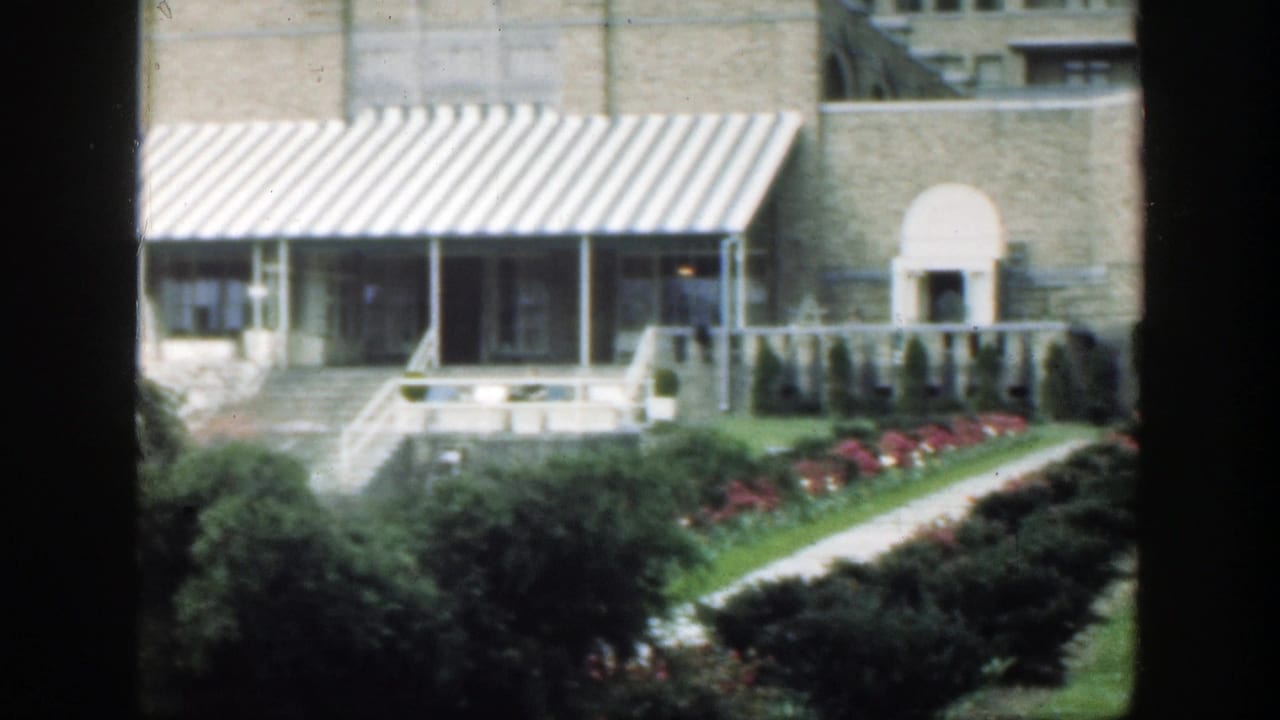 Building frontage with striped awning, arched doorway, shrubs, flowers, and a diagonal garden path.