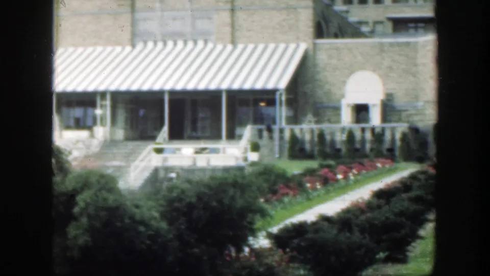 1949 Cincinnati frame with a striped awning across a masonry frontage, an arched doorway, hedges, flowers, lawn, and a walkway.