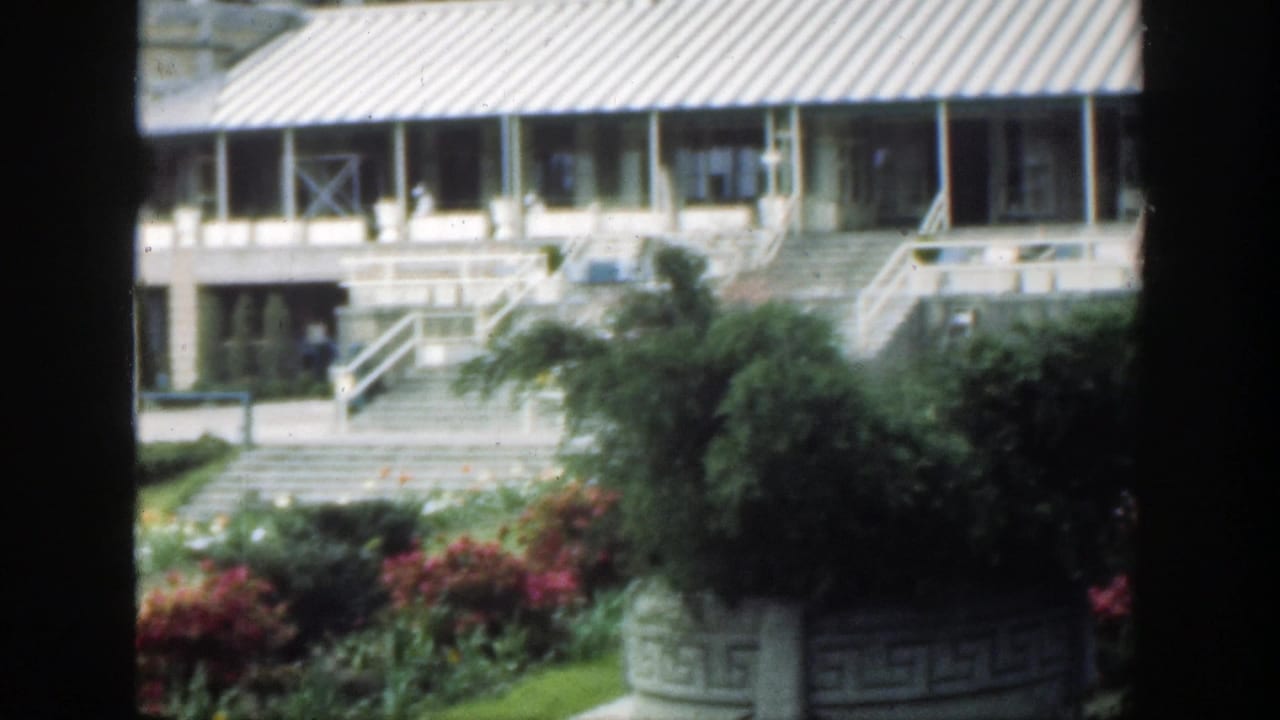 Garden beds and lawn in front of a building, seen through dark vertical frame edges.