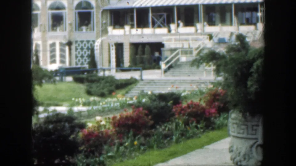 A Cincinnati garden scene shows a building entrance, broad steps, flowers, and a large planter in soft 1949 8mm color.
