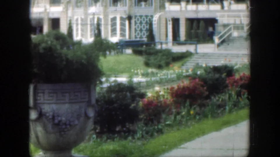 The 1949 Cincinnati footage looks across a flower garden and walkway toward a building, with dark frame edges crossing the view.