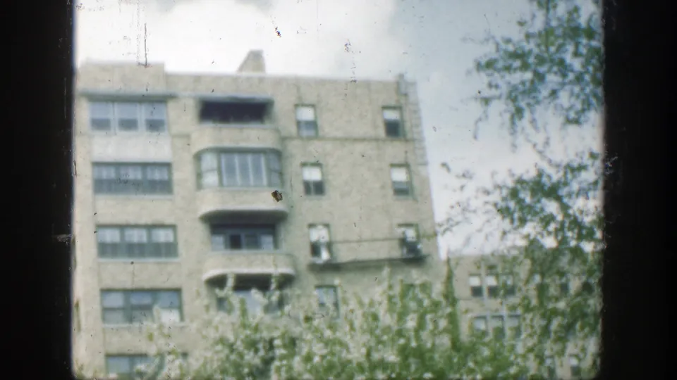 A soft 8mm view in Cincinnati shows a multi-story building facade partly screened by trees and foreground foliage.