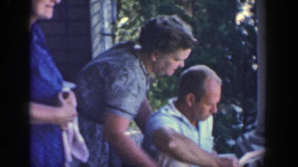 In 1964 Wisconsin home-movie footage, a seated man and two older women gather on a porch, focused on something below frame.