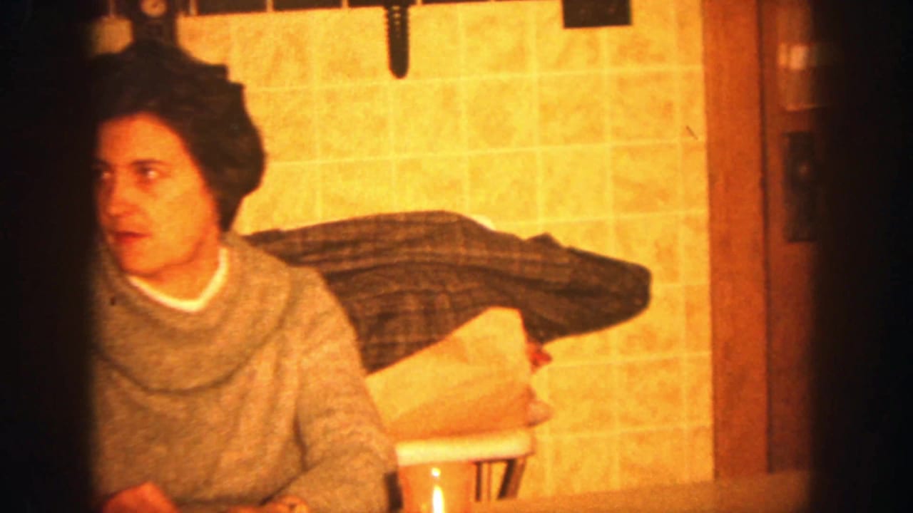 Woman in a gray sweater sits at a kitchen table near a red cup and paper bag.