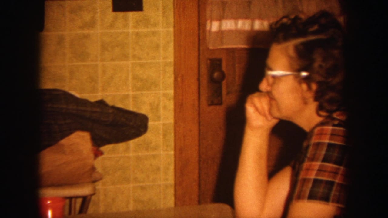 Woman in plaid shirt and glasses rests her chin on her hand in a kitchen interior.