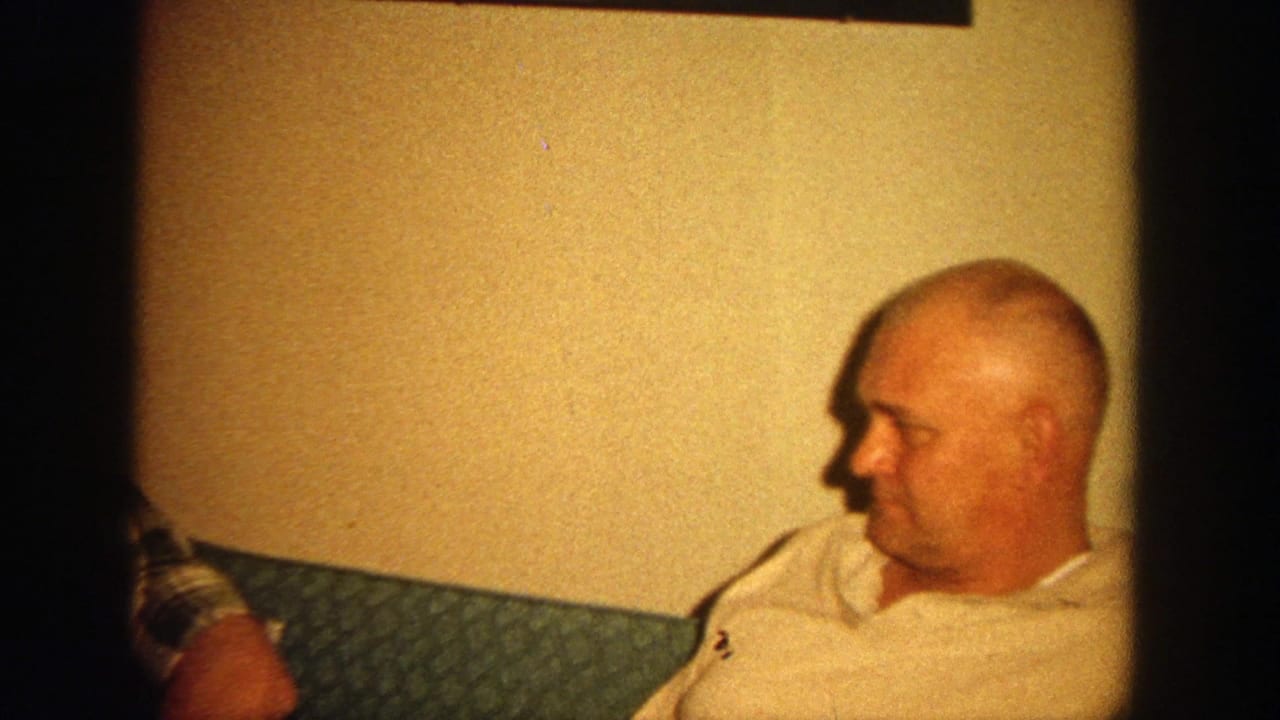 Two adult men sit on a green couch in a warmly lit living room.
