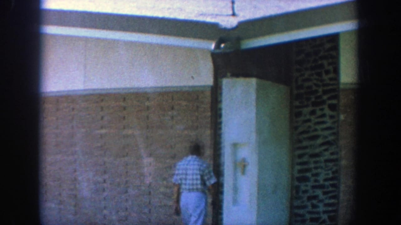 Man in a blue checkered shirt walking beside tan brick and stone walls.
