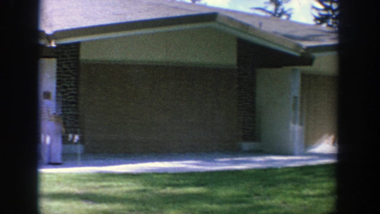 Wisconsin 1964 frame of a mid-century church or tabernacle exterior with a low roof, brick column, stucco walls, and lawn.