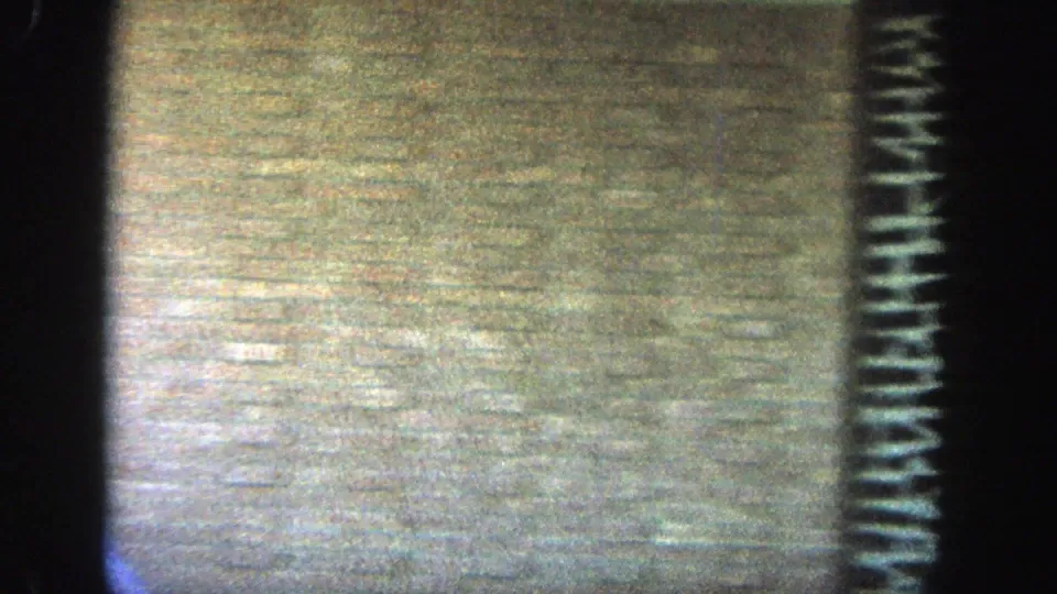 1964 Wisconsin 8mm frame showing the textured tan brick building facade and dark decorative stonework after the walkers move out of view.