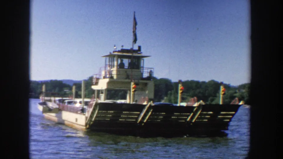 1964 Wisconsin 8mm view of a ferry moving across blue water, framed by dark film edges with the wooded shoreline behind it.