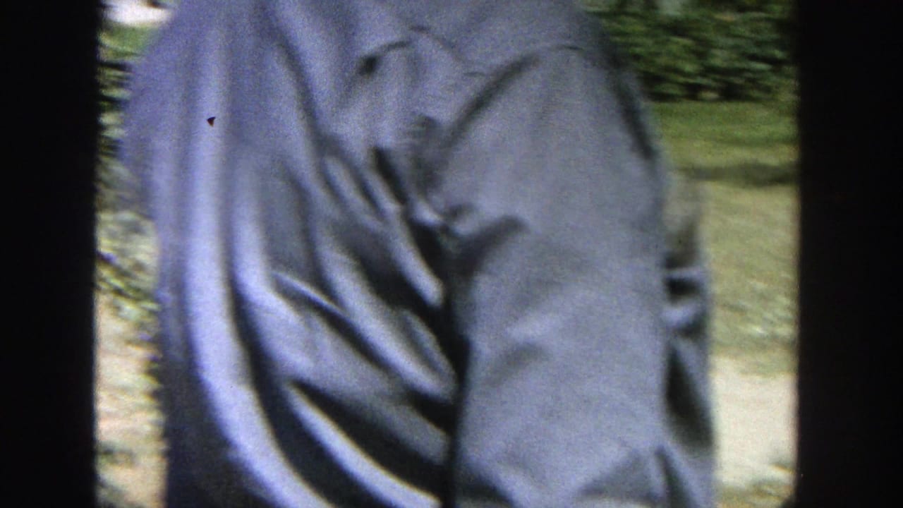 A man in a light blue shirt is partly seen from behind near apple trees in the Wisconsin home-movie footage.
