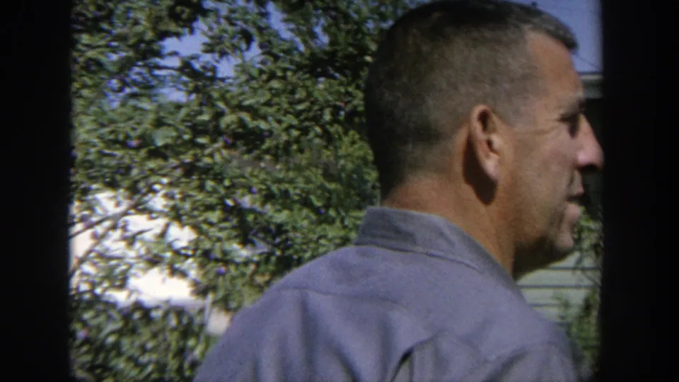 A middle-aged man appears in profile near trees and a small structure in the 1964 Wisconsin orchard scene.