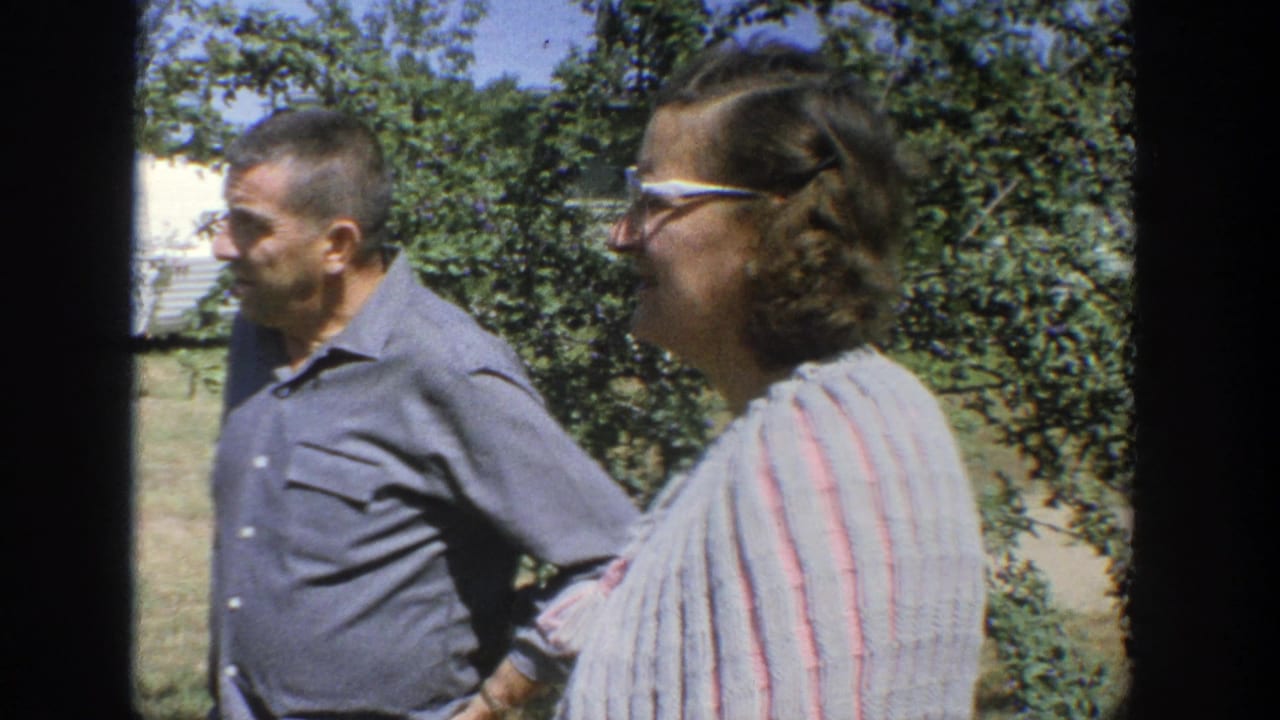 Man and woman walking outdoors beside trees and grass.