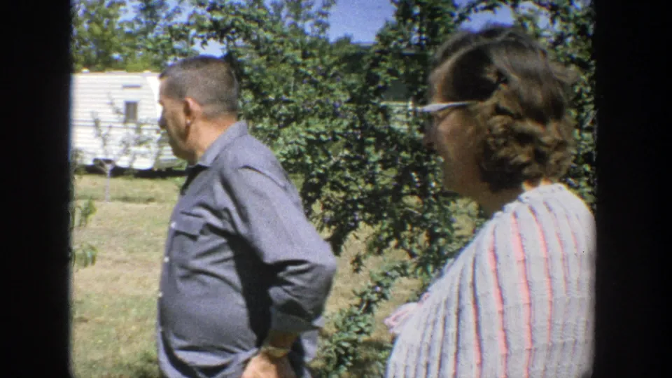 A close side view shows the man and woman walking beside leafy trees in the 1964 Wisconsin home-movie scene.