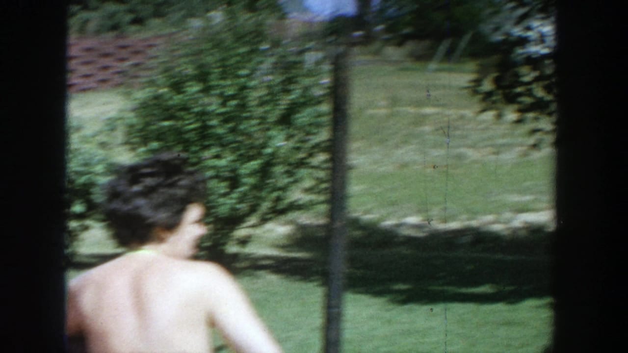 Woman seen from behind crossing a sunny lawn near hedges.