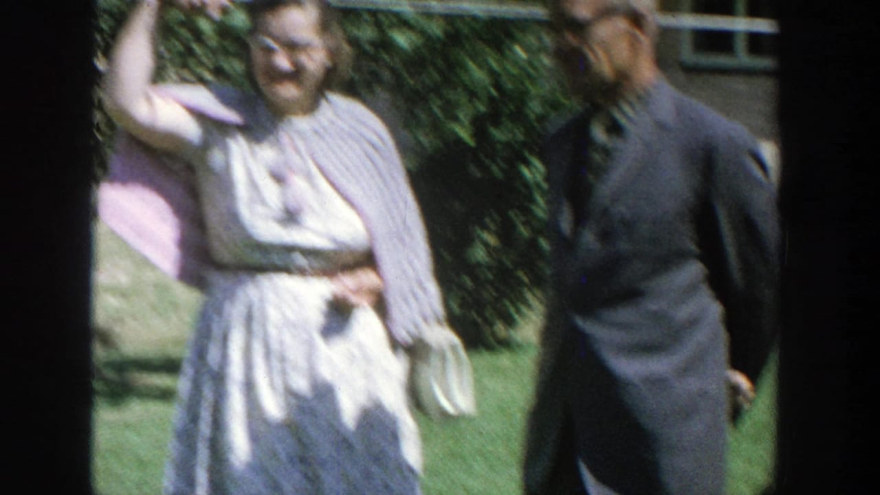 Woman in a light dress stands beside a man in a dark suit outdoors.