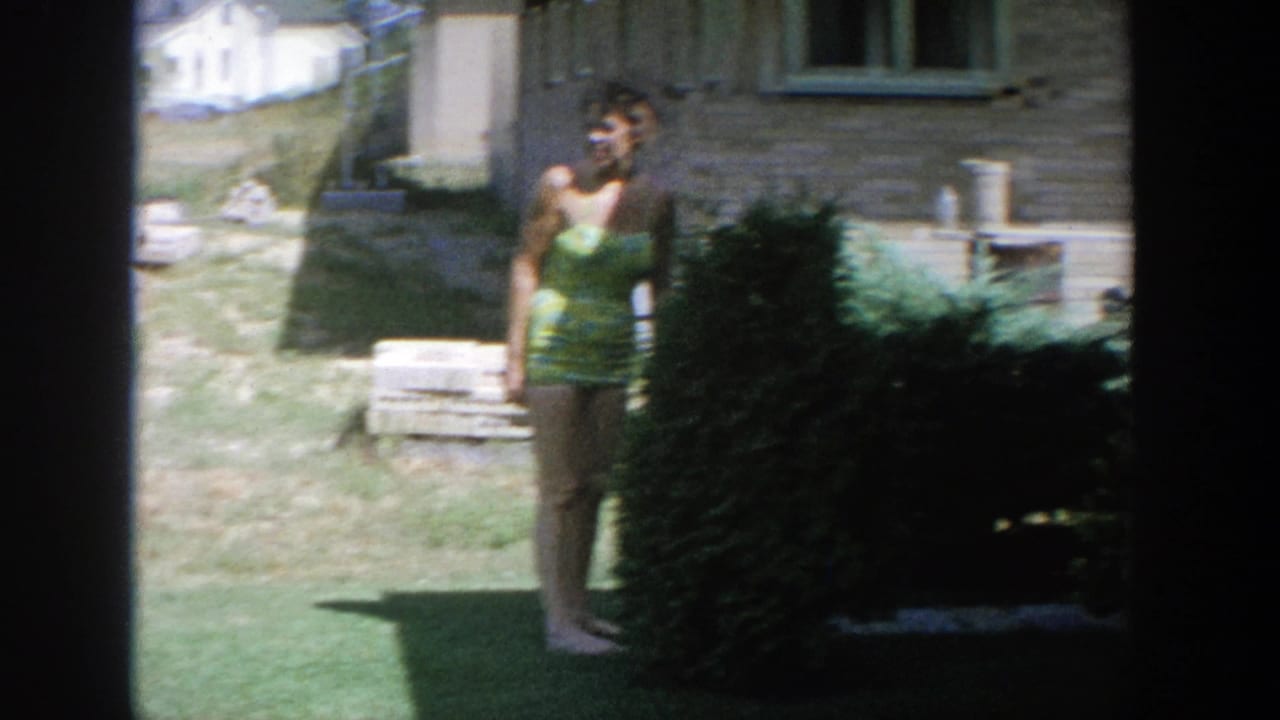 Woman in a green swimsuit smiles toward the camera while standing by a large shrub.