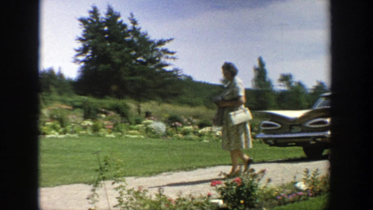 Woman with white handbag walking on a path beside a lawn and classic car.