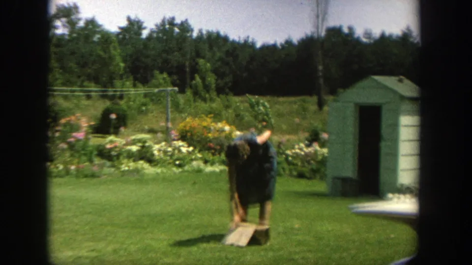 Later in the clip, a person bends near the grass by a garden bed and small shed in the Wisconsin yard.