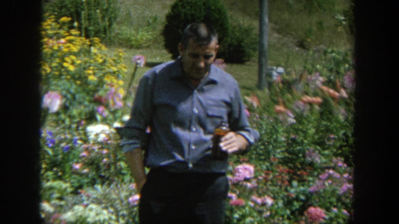 Adult man in a blue shirt standing among flowers and garden greenery.