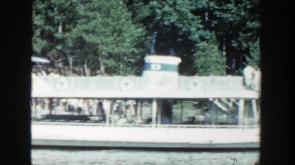 Side-on 1964 Wisconsin 8mm frame of a white tour boat, showing rows of passengers beneath an open-sided canopy.