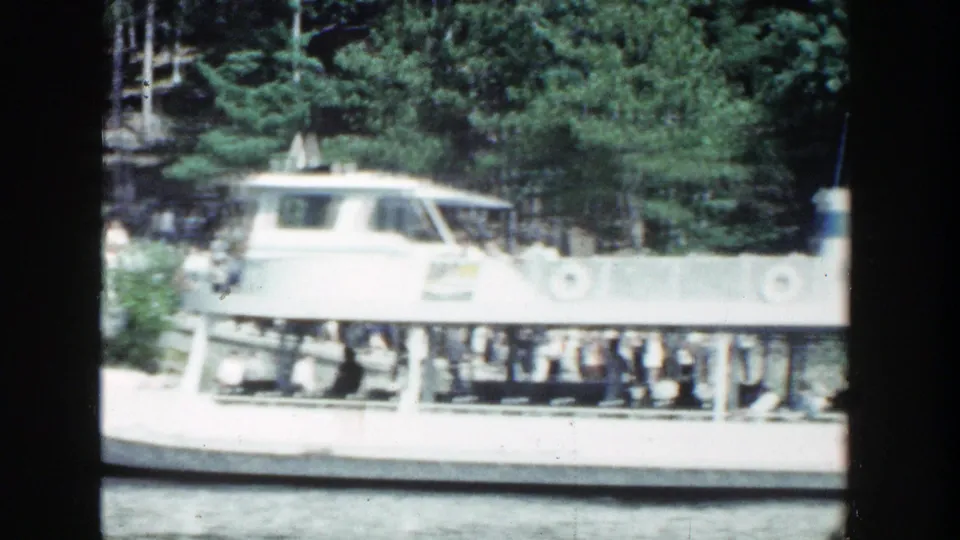 A white sightseeing boat filled with passengers moves through a wooded Wisconsin river scene in soft 8mm color.