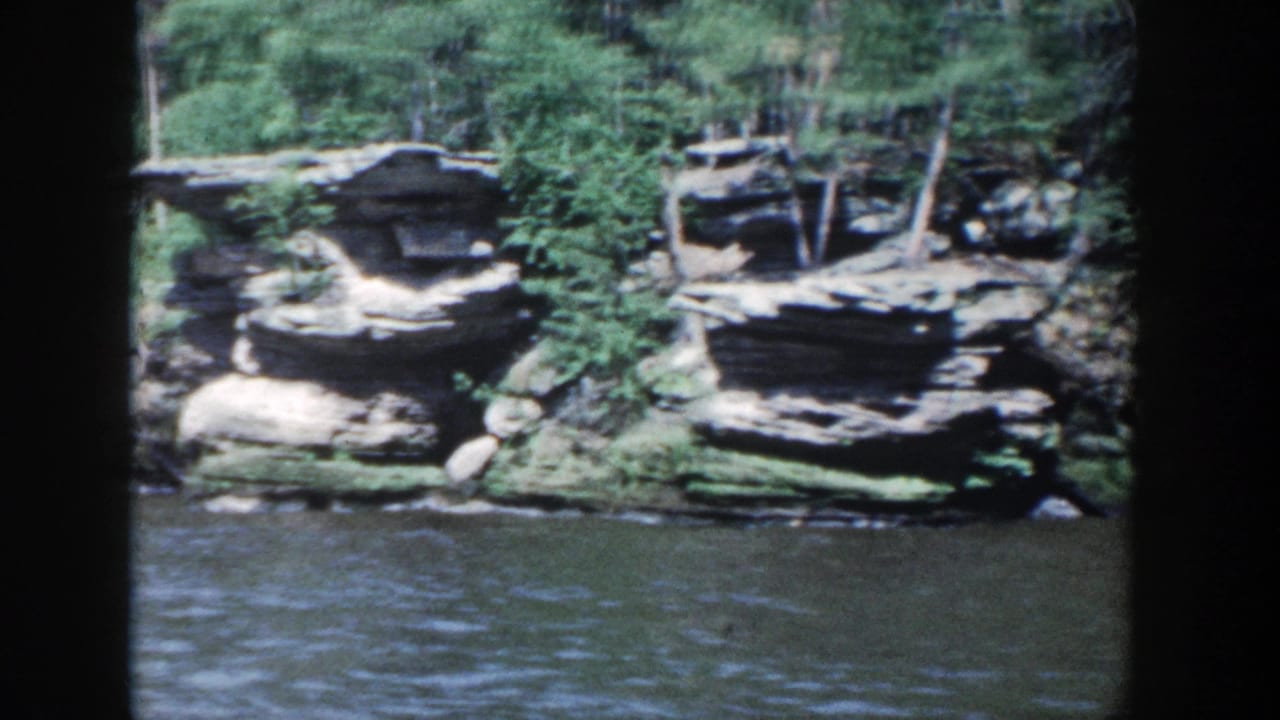 Layered rock ledges and dense trees above calm river water.