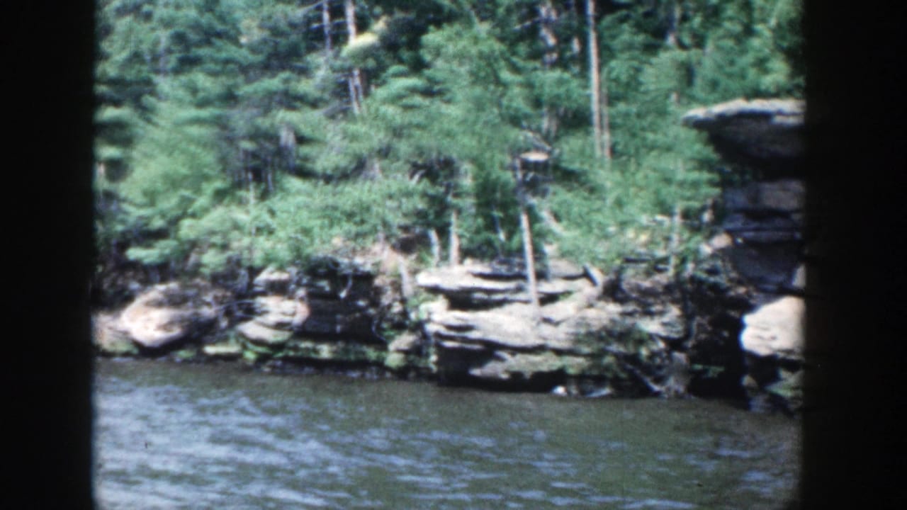 Rocky river shoreline with trees above rippling water.