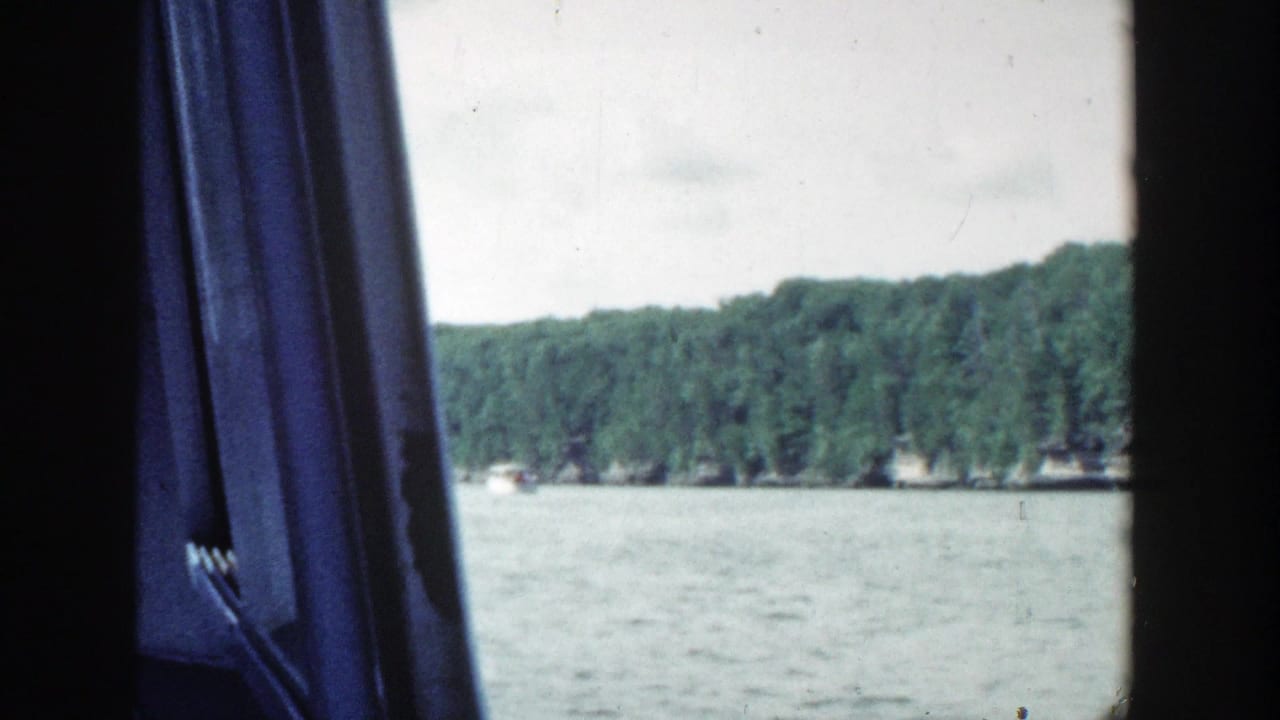 Wooded lakeshore and water viewed past a blue curtain and dark interior framing.