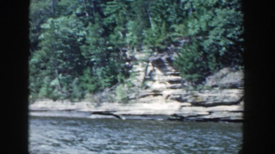 Wisconsin lake shoreline with rock formations, dense trees, and rippled water in 1964 8mm home-movie footage.