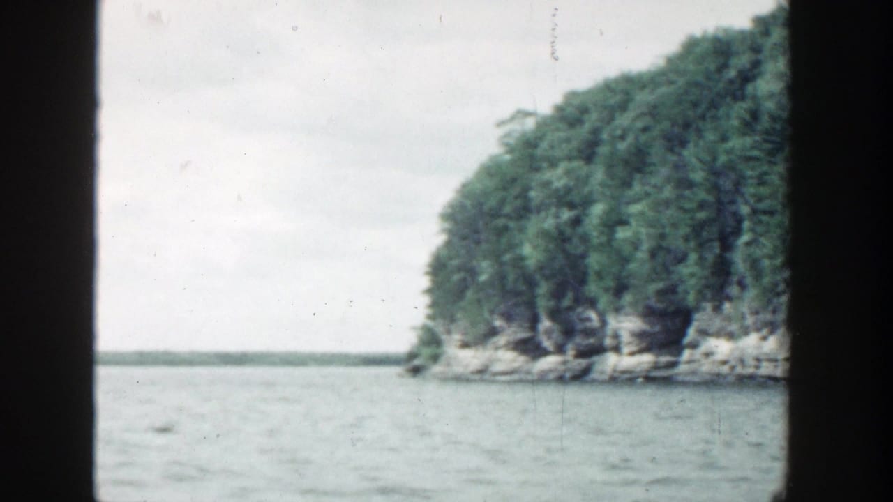 Rocky, forested point beside open water with film frame edges visible.