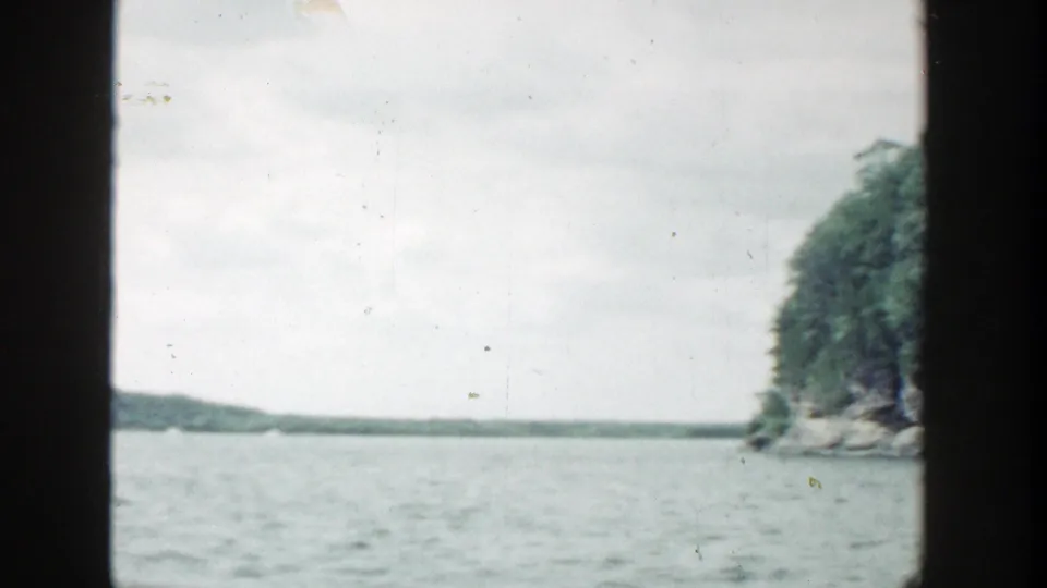 1964 Wisconsin 8mm frame looking over rippled water toward low distant land and a wooded rocky edge at right.