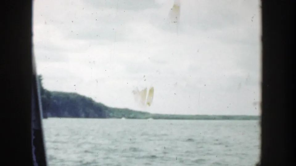 1964 Wisconsin 8mm frame showing a wide water view, distant low shoreline, and wooded rock face near the right edge.