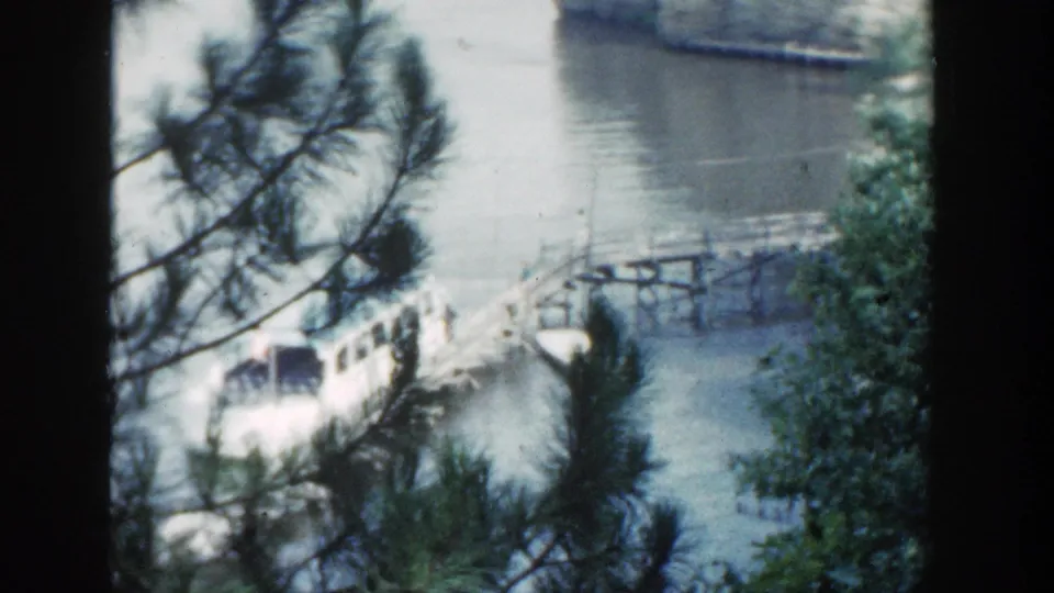 The white lake tour boat remains beside the wooden dock, with trees and a pale rock face visible across the water.