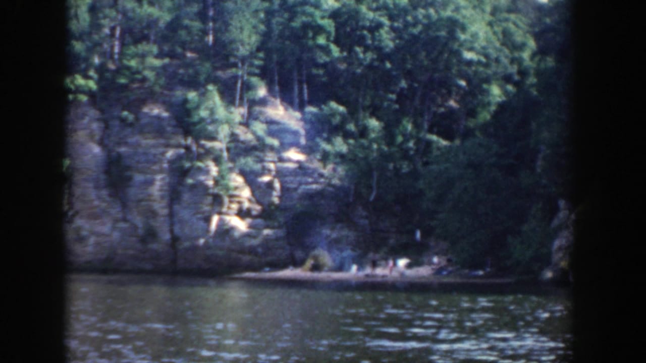 Forested rock cliff across a river with dark film borders.