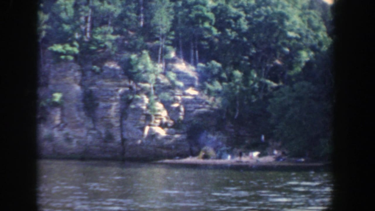A similar 1964 Wisconsin river view, with trees above a pale rock face and water filling the foreground.