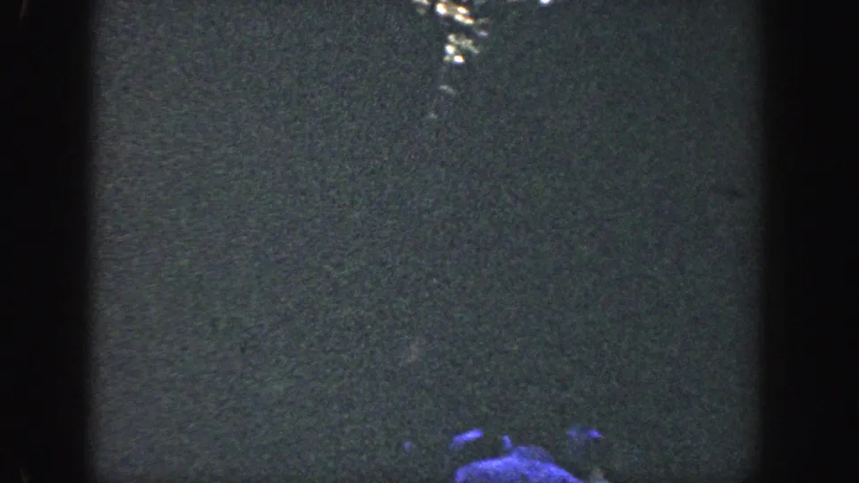 Low-exposure 1964 Wisconsin 8mm frame with rippled water and a partial blue-tinted person at the bottom.