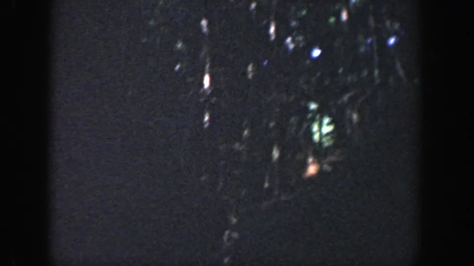 1964 Wisconsin 8mm frame showing a dark forest area with faint reflected highlights and no clear human figure visible.
