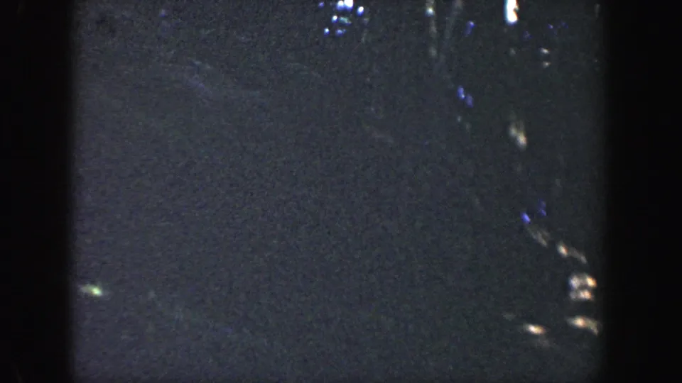1964 Wisconsin 8mm frame showing a dark wooded area with faint foliage, light streaks, and no clearly identifiable face.